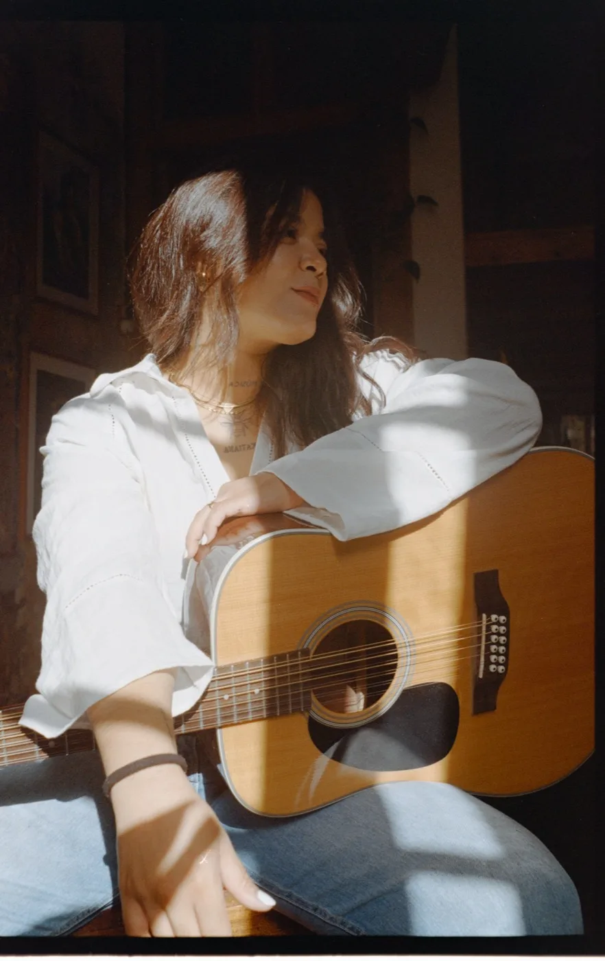 Nadieska sentada con una guitarra de doce cuerdas, con la luz del sol cruzándole la cara.